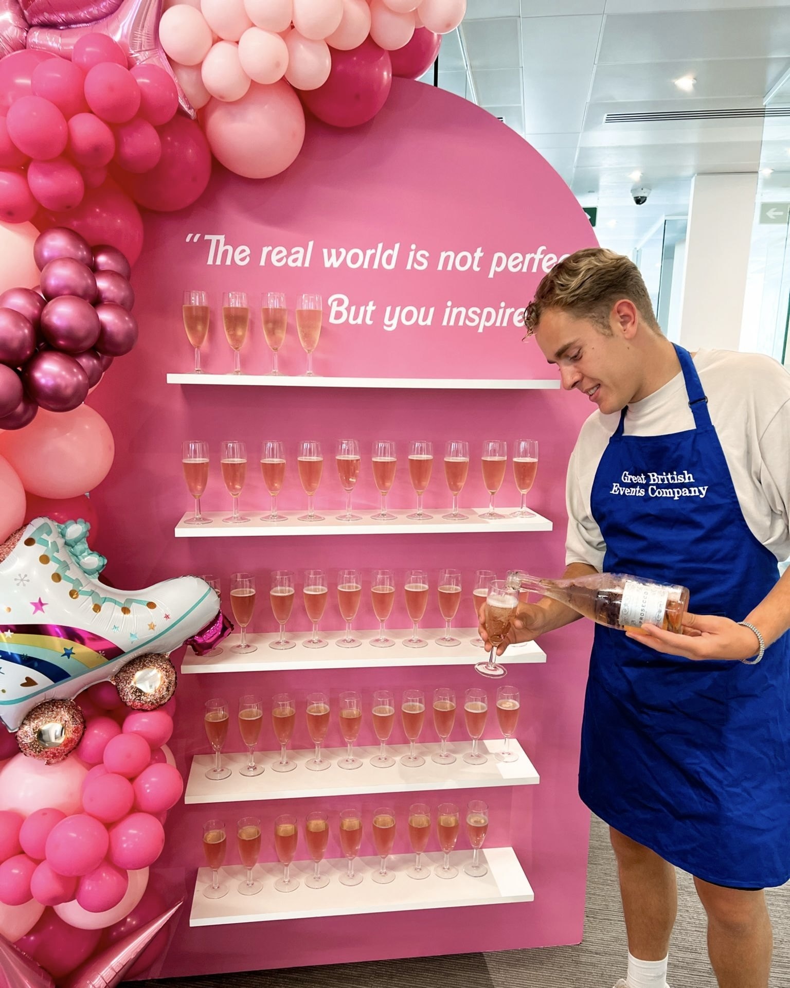 Great British Events Co staff member pouring a drink beside a pink drinks wall.