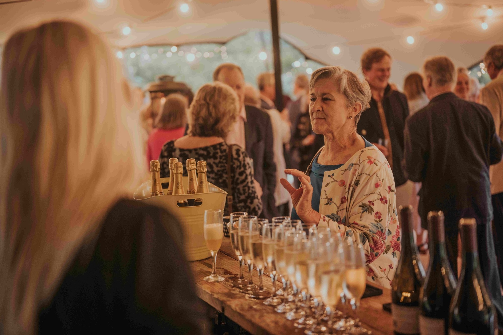 Guests enjoying drinks at a wooden event bar beneath a stretch tent.